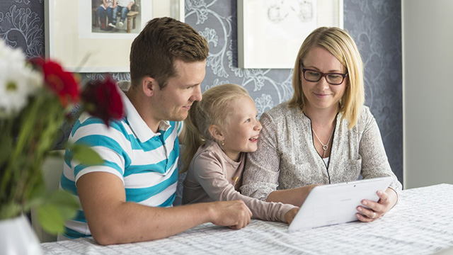 Kolmehenkinen perhe istuu pöydän ääressä ja katsoo kannettavaa tietokonetta.